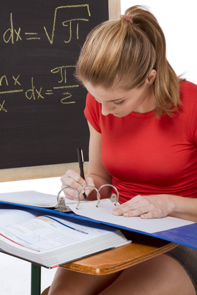 High school or college female student sitting by the desk at math class. Blackboard with advanced mathematical formals is visible in background